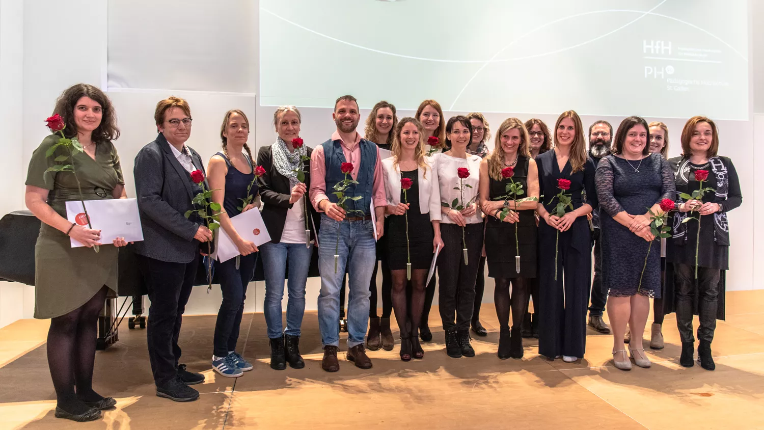 Gruppenbild: Absolventinnen und Absolventen des Masterstudiengangs Schulische Heilpädagogik halten ihr Diplom plus Rose; feierlicher Anlass; stehen auf Bühne (Foto: PHSG); 